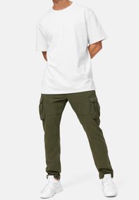 Valkoinen lyhythihainen puuvillainen t-paita, yhdistetty oliivinvihreisiin cargo-housuihin, joissa on etu- ja sivutaskut, viimeistelty valkoisilla tennareilla.