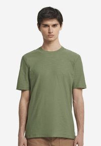 Grön kortärmad t-shirt av texturerat tyg, med rund halsringning och avslappnad passform, visad på en enkel bakgrund.