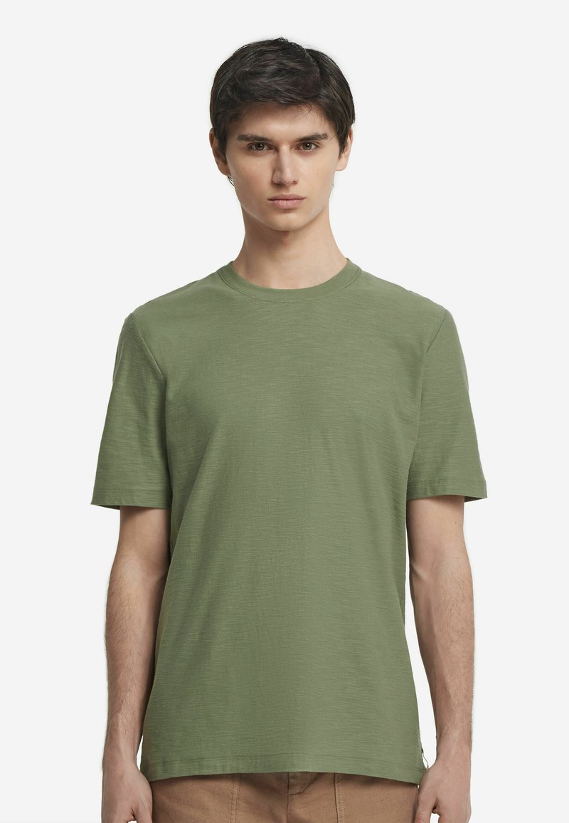 Grön kortärmad t-shirt av texturerat tyg, med rund halsringning och avslappnad passform, visad på en enkel bakgrund.