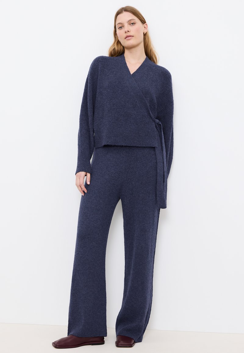 Granatowy dzianinowy sweter z wiązaniem, połączony z pasującymi szerokimi spodniami, obie części o miękkiej, teksturowanej fakturze.