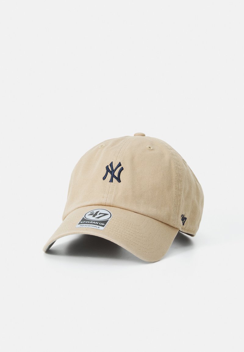Beige bomullsbaseballcap med en marineblå brodert logo, med buet skygge og justerbar stropp. Inkluderer et merke på fronten.