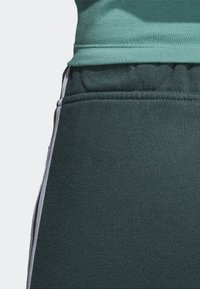 Dark green sweatpants with elastic waistband, side pockets, and contrasting white stripes down the outer seams. Soft fabric texture.