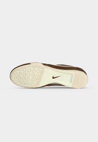 Σόλα καφέ και μπεζ παπουτσιού Nike με υφή λαβής στη μύτη και λογότυπο Nike swoosh κοντά στην περιοχή της καμάρας.