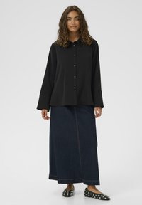 Juodas marškinėliai su apykakle, ilgomis rankovėmis, derinami su tamsiai mėlynomis džinsinio audinio maksi sijonais, turinčiais priekinius siūlėms ir kontrastingas siūles.