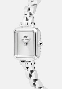 Montre rectangulaire en argent avec un cadran minimaliste et deux aiguilles. Le bracelet en acier inoxydable présente une texture lisse et polie.