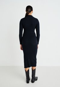 Form-fitting, long-sleeve, ribbed knit dress in dark navy, extending to mid-calf, paired with leather cowboy-style boots.
