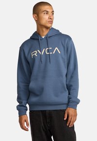 Felpa blu con tasca a canguro frontale e cappuccio con coulisse. Presenta il logo "RVCA" di colore crema stampato sul davanti. Materiale in mistura di cotone.