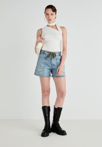 White sleeveless top with shoulder tie, denim shorts with frayed hem and green drawstring, and knee-high black lace-up boots.
