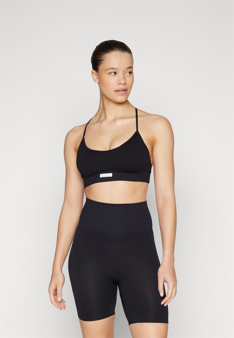 Black ribbed sports bra with adjustable thin straps, paired with high-waisted ribbed bike shorts, sleek texture, minimalist style.