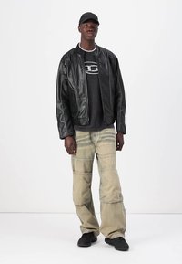 Jachetă bomber din piele neagră peste un tricou negru, asortată cu pantaloni cargo largi de culoare deschisă și adidași negri. Accesoriu: șapcă neagră.
