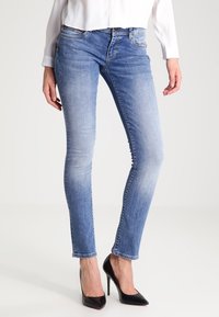 Jasnoniebieskie dżinsy skinny z wyblakłym wzorem, pięć kieszeni, przyszywane akcenty; zestawione z czarnymi szpilkami.