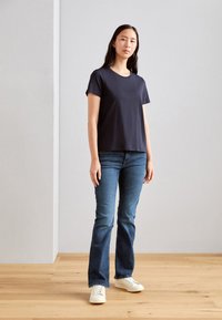 Granatowa koszulka bawełniana z krótkim rękawem, zestawiona z ciemnoniebieskimi dżinsami i białymi sneakersami. Prosty design, luźny krój, minimalistyczne detale.