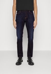 Tmavě modré džíny z denimu s rovnými nohavicemi, designem s pěti kapsami a detaily v oranžovém prošívání. Vydáno s černými šněrovacími botami.