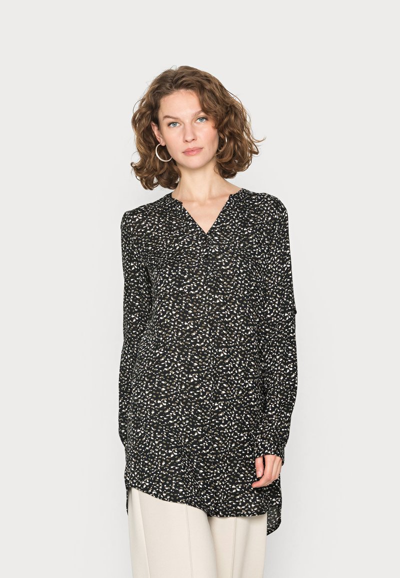 Camisa tunica preta com um padrão abstrato branco, decote em V, mangas longas e um ajuste ligeiramente solto. Feita de tecido leve.