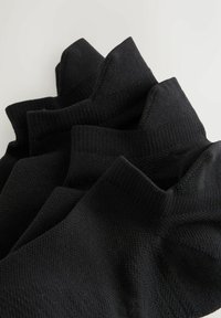 Los calcetines negros presentan un tejido de punto texturizado, puños acanalados y un acabado suave. Están apilados, mostrando diferentes alturas y contornos.