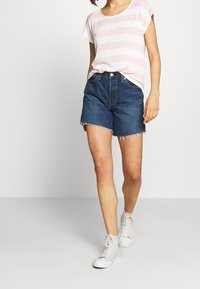 Denim shorts in dark blue with frayed hem, paired with a light pink striped T-shirt and white high-top sneakers. Casual ensemble.