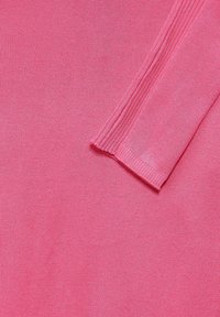 Růžová pletená tkanina s hladkou texturou, se žebrovaným akcentem podél okraje a zblízka zachyceným detailem šití.