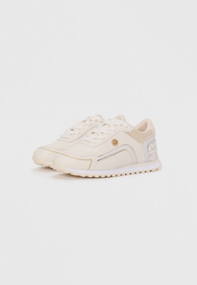 Baskets de sport beige avec une tige synthétique lisse, des accents en maille, des lacets plats et une semelle texturée présentant un design à motifs.