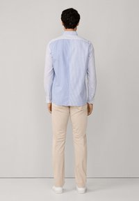 Lichtblauw en wit gestreepte lange mouwen shirt met een kraag met knopen, gecombineerd met beige broeken en witte schoenen.