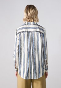 Camicia a maniche lunghe a righe in bianco, blu e nero. Presenta un colletto a punta, polsini con bottone e orlo arrotondato. Tessuto morbido.