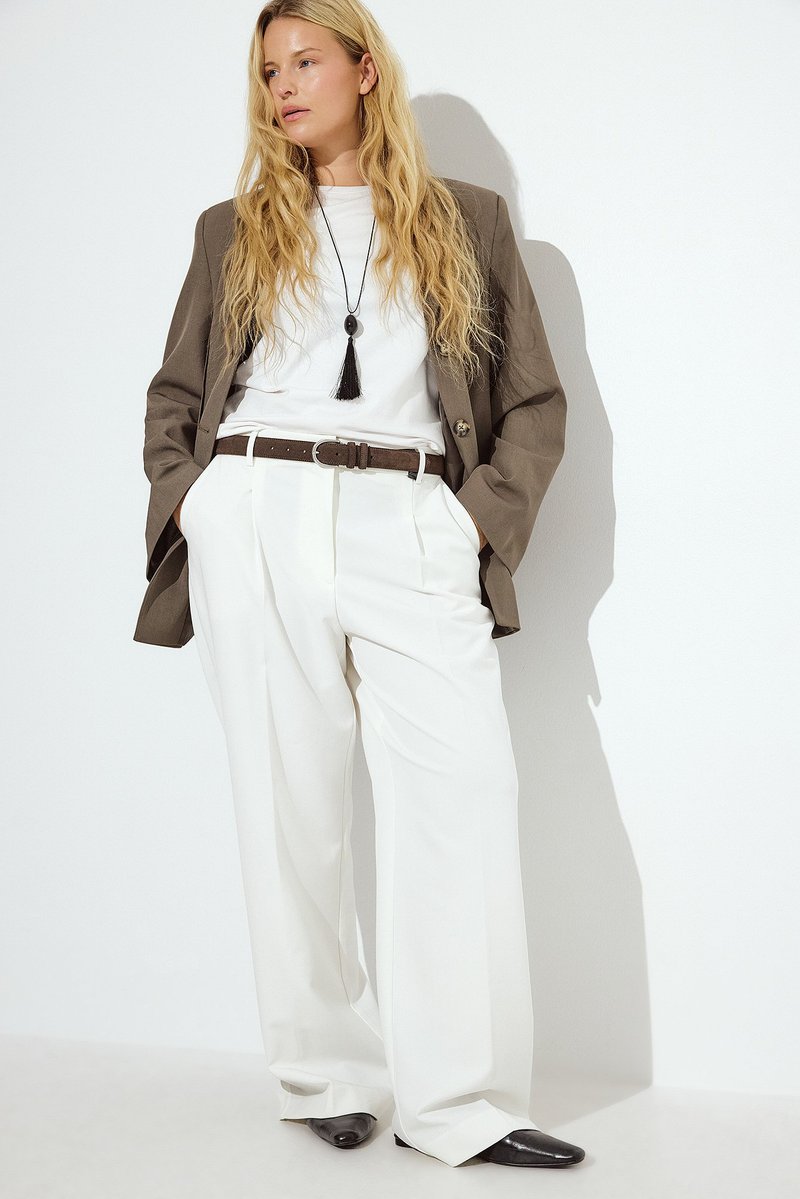 White pleated trousers paired with a gray blazer over a white T-shirt, accented by a brown belt and black pointed shoes.