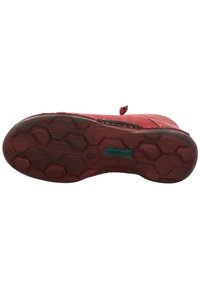 Chaussure en daim rouge avec une semelle en caoutchouc texturé présentant un motif hexagonal et un logo de marque vert. Le système de laçage comprend une petite boucle.