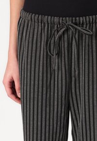 Pantalons rayés noir et blanc avec une taille élastique à cordon de serrage, présentant une texture douce et des lignes verticales étroites pour une apparence élégante.
