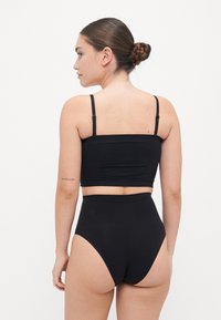 Fekete crop top és magas derekú alsó sima, nyújtható anyagból. Vékonyan állítható pántokkal és szoros illeszkedéssel rendelkezik, minimalizált varrásokkal.