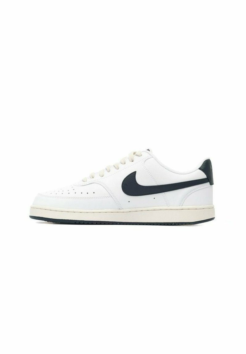 Zapatilla de cuero blanca con el swoosh negro de Nike, puntera redonda, detalles perforados, cordones planos y una suela de goma texturizada.