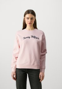 Felpa rosa con polsini e orlo a coste, caratterizzata dal logo "Tommy Hilfiger" ricamato in blu navy sul petto. Texture morbida, vestibilità rilassata.