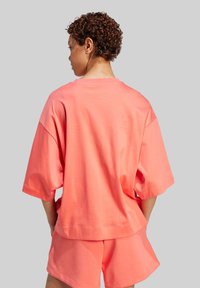 Korálová voľná tričko s krátkym rukávom a uvoľneným strihom, vyrobené z mäkkej bavlnenej látky. V kombinácii s zodpovedajúcimi šortkami.