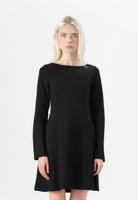 Svart langermet kjole med båtutringning, tettsittende liv og utskjært skjørt. Glatt tekstur, ingen synlige mønstre eller dekorasjoner.