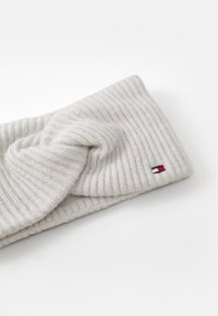 Light gray knitted headband with a twisted design and ribbed texture, featuring a small embroidered logo in red, white, and blue.