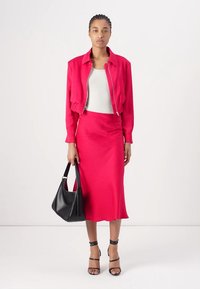 Fuchsia cropped bomber jacket, white fitted tank top, and matching fuchsia midi skirt. Model carries a black shoulder bag and wears black sandals.