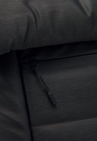Gros plan d'une surface en tissu noir avec une petite poche zippée et une fine languette de tirette en tissu.