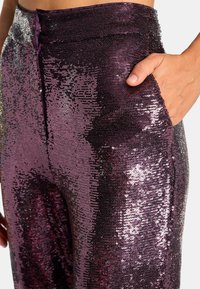Spodnie z cekinami w odcieniach fioletu i srebra, charakteryzujące się dopasowanym krojem, gładką fakturą oraz boczną kieszenią dla zwiększenia funkcjonalności.