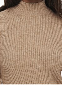 Beżowy prążkowany sweter typu turtleneck o dopasowanym kroju. Teksturowany materiał z subtelnymi wariacjami w tonacji i wysokim dekoltem.
