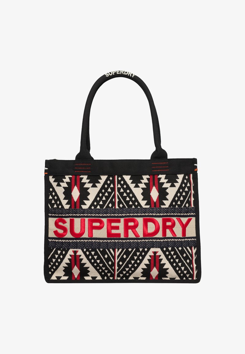 Sac fourre-tout noir et crème à motifs avec le texte rouge "SUPERDRY". Présente des designs géométriques et des poignées noires. Fabriqué en tissu durable.