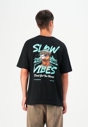 Black cotton t-shirt featuring a graphic of a camel wearing sunglasses and a beanie, with the text "SLOW VIBES" and "Don't Get The Hump."