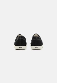Zwarte suède sneakers met witte stiksels en rubberen zolen, met een logo op de hiel. Laag ontwerp met een afgeronde vorm.