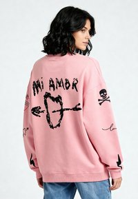 Felpa oversize rosa con grafiche nere, inclusi testi "Mi Amor", teschi, cuori e frecce. Tessuto morbido e testurizzato.