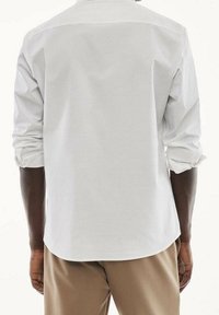 Weißes Langarmhemd mit Rückenteil, geknöpften Manschetten und geschwungenem Saum. Glatter Stoff mit lockerem Schnitt und hochgekrempelten Ärmeln.