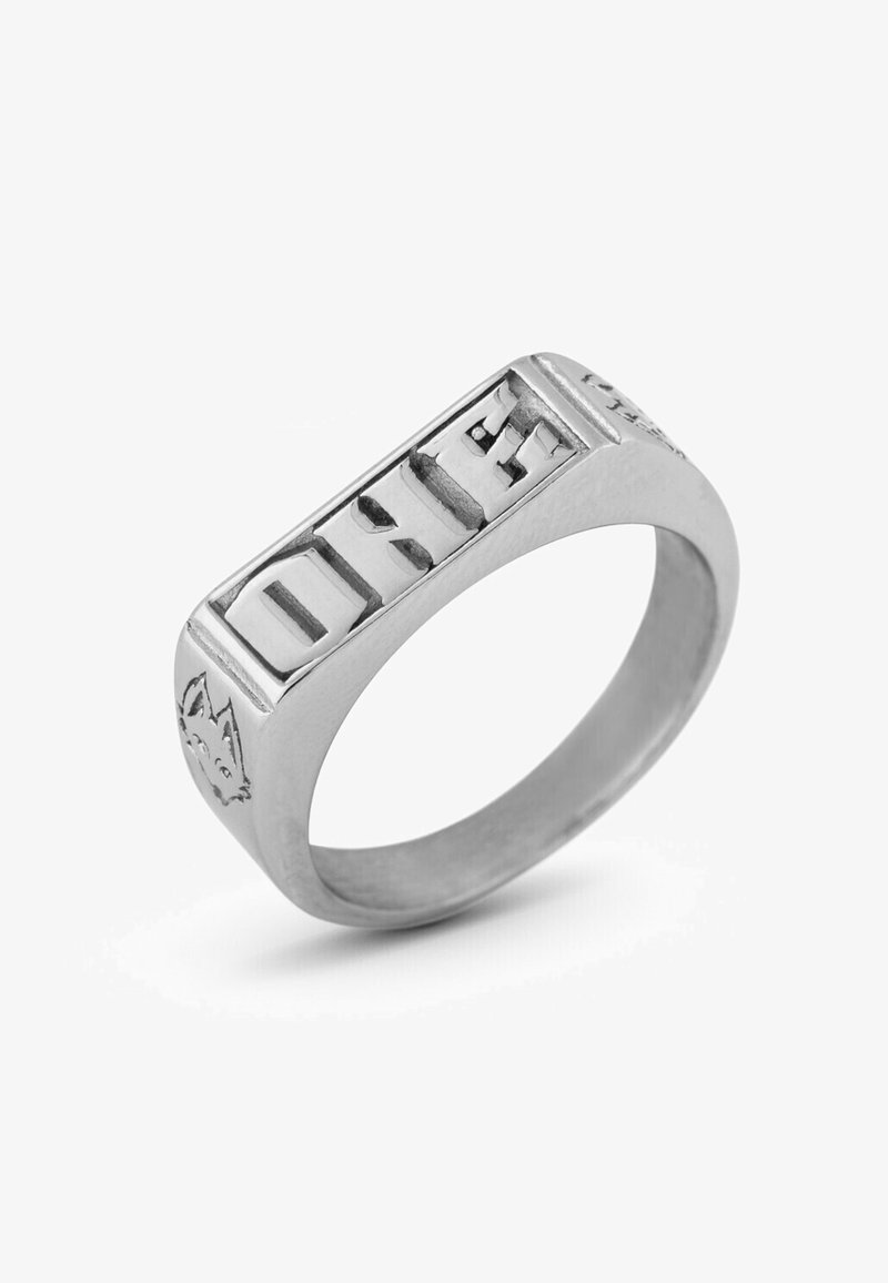 Bague en métal argenté avec un visage rectangulaire présentant le mot "UN" gravé. Le côté arbore un design détaillé d'un visage de loup. Texture lisse, finition polie.