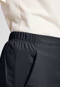 Zwarte elastische tailleband van sportbroeken, met een gladde stofstructuur en gestikte details langs de zijnaad, gecombineerd met een licht shirt.