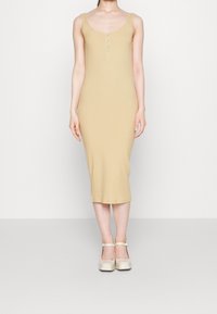 Žebrované šaty po kolena v sv ětlé béžové barvě s lodičkovým výstřihem a knoflíkovou légou na pět knoflíků. Modelka doplnila obuví s tenkými pásky v jemné barvě.