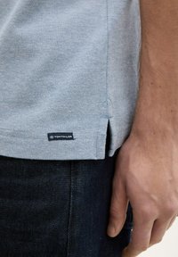 Lichtblauwe shirt van een geweven stof, met een zijsplit en een zwart "TOM TAILOR" label. Gecombineerd met donkerdenim jeans.