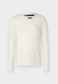 Bílý svetr s V výstřihem a dlouhým rukávem, na levé části hrudi s malým logem Tommy Hilfiger v červené, bílé a modré barvě.