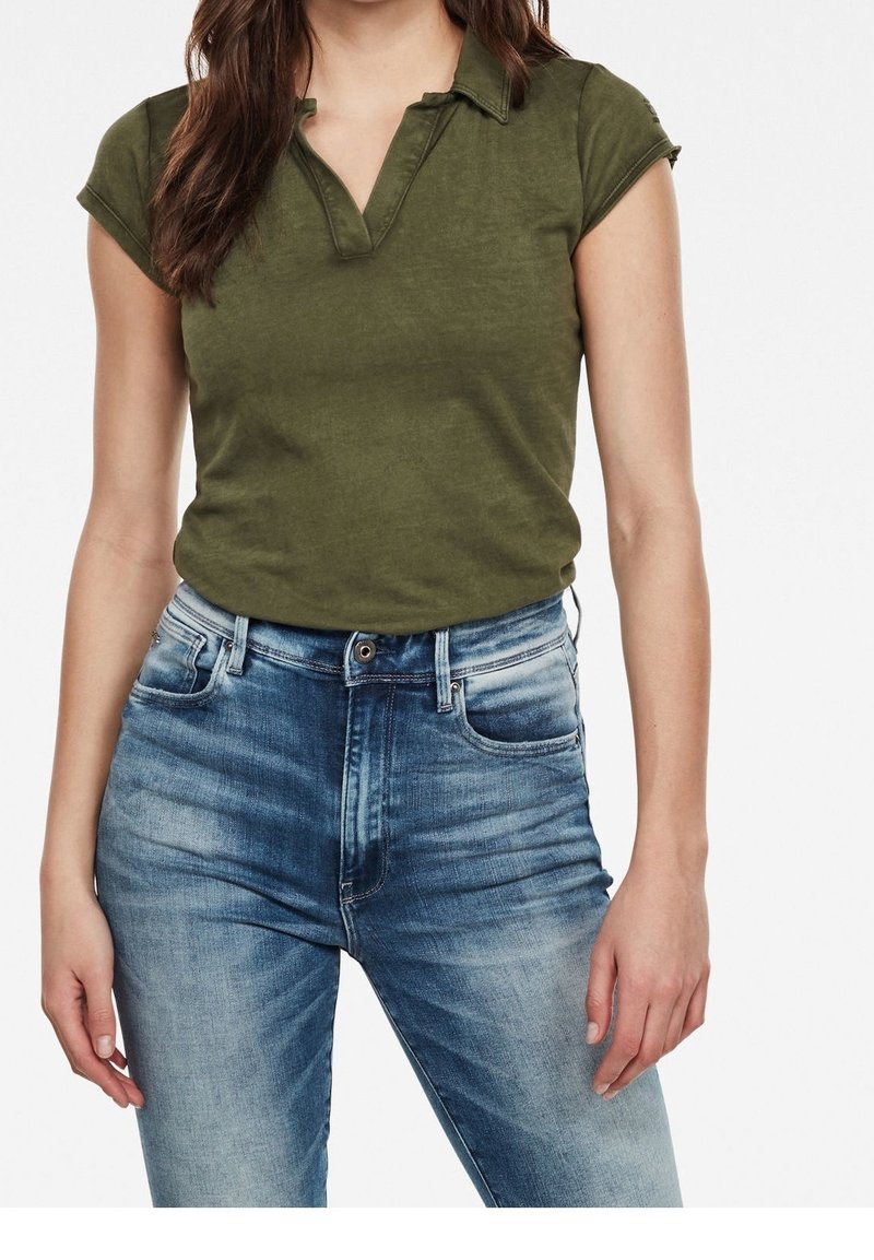 Olivgrön pikétröja med kort krage och vikta ärmar, tillsammans med medelblå jeans i denim med klassisk passform.