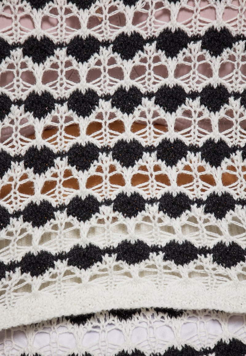Spitzenstoff mit abwechselnd schwarzen und weißen kreisförmigen Mustern, ausgestattet mit filigranen Durchbrüchen und einer weichen, strukturierten Oberflächenbeschaffenheit.