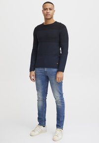 Marine gestreepte gebreide trui met ronde hals, gecombineerd met lichtblauwe slim-fit jeans en witte sneakers. De textuur is glad met een casual ontwerp.